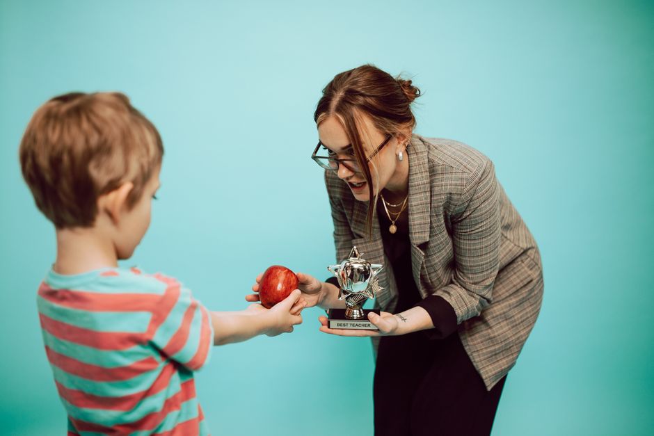 A child offers an apple to a teacher holding a 