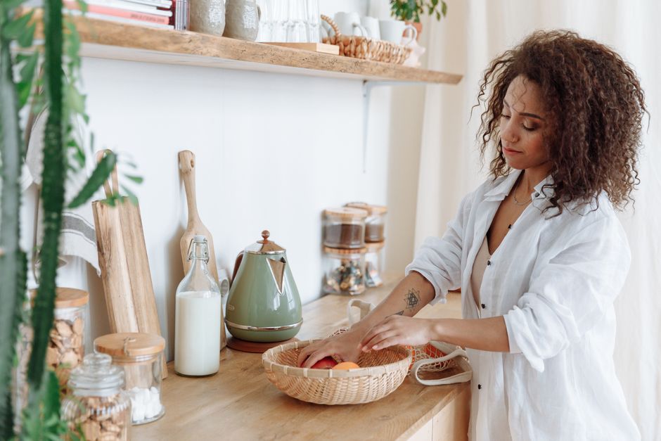 A woman with curly hair arranging fresh fruits in a modern kitchen space.
