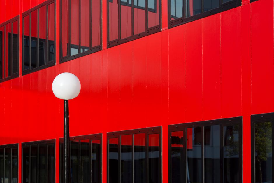 Striking red building facade featuring glass windows and a sleek white lamp post.