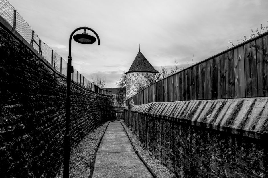 A scenic view of a stone tower and pathway in Switzerland, captured in monochrome.