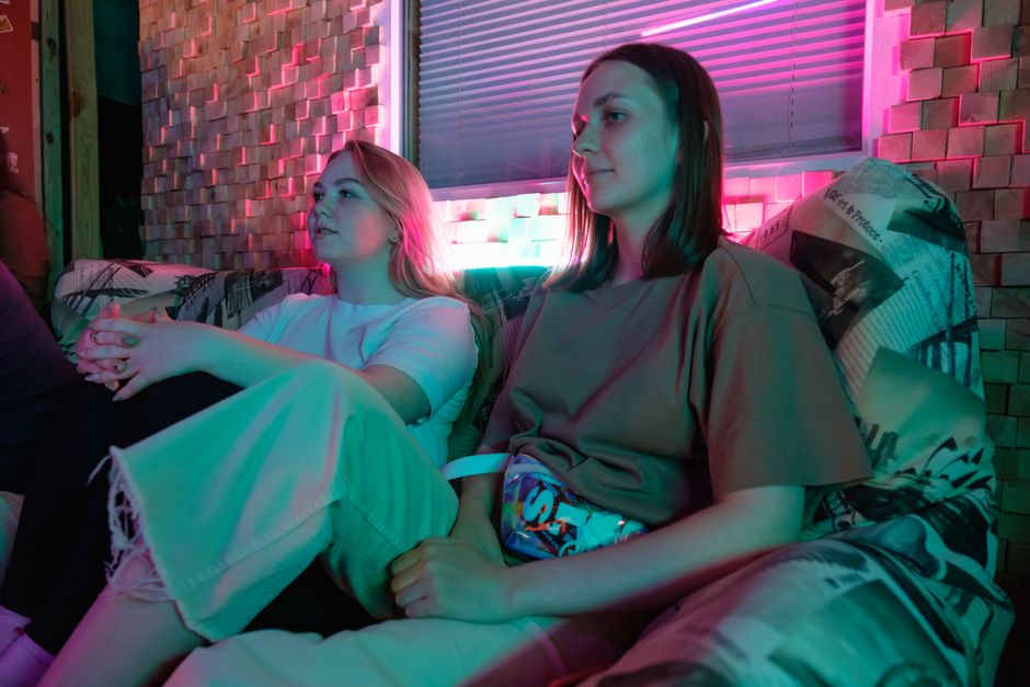Two women relaxing indoors in neon lighting, creating a cozy and modern ambiance.
