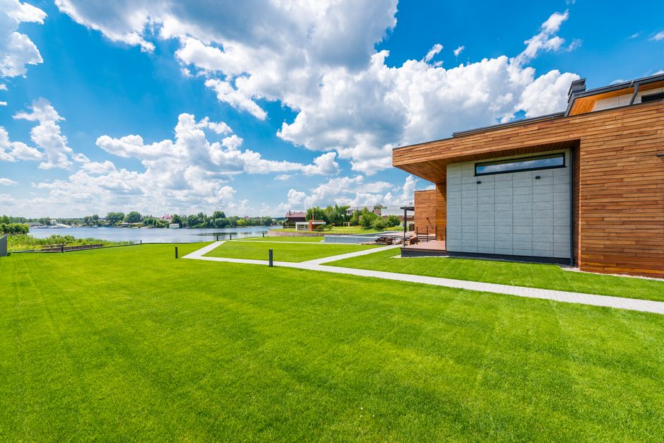 Landscape with modern building on grassy lawn and lake and forest in background against cloudy sky