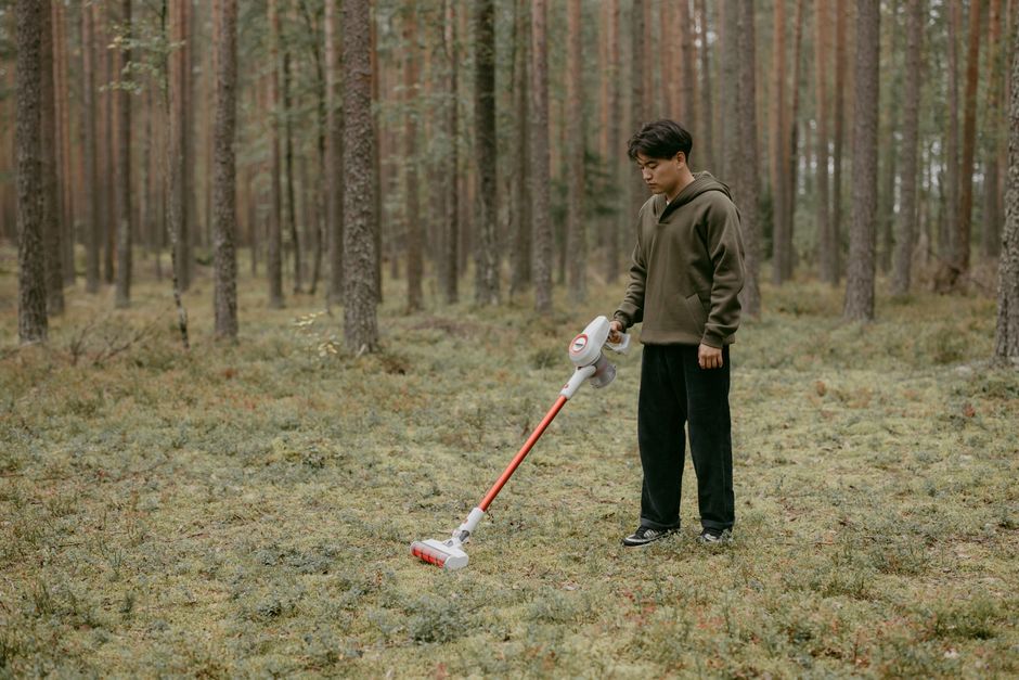 An adult man with a vacuum cleaner in a forest setting, capturing modern living concepts.